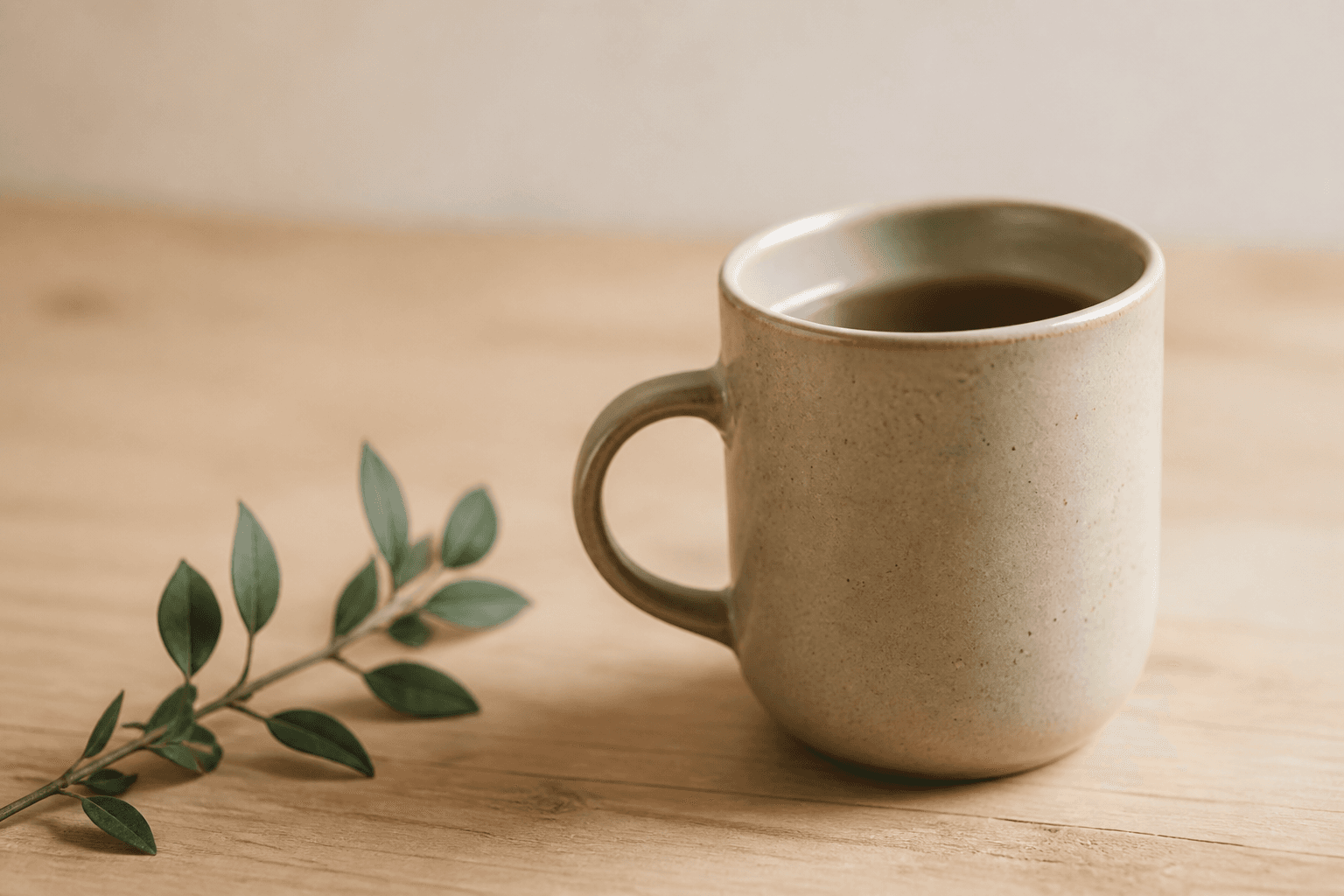 A ceramic mug beside a leafy sprig on a wood table
