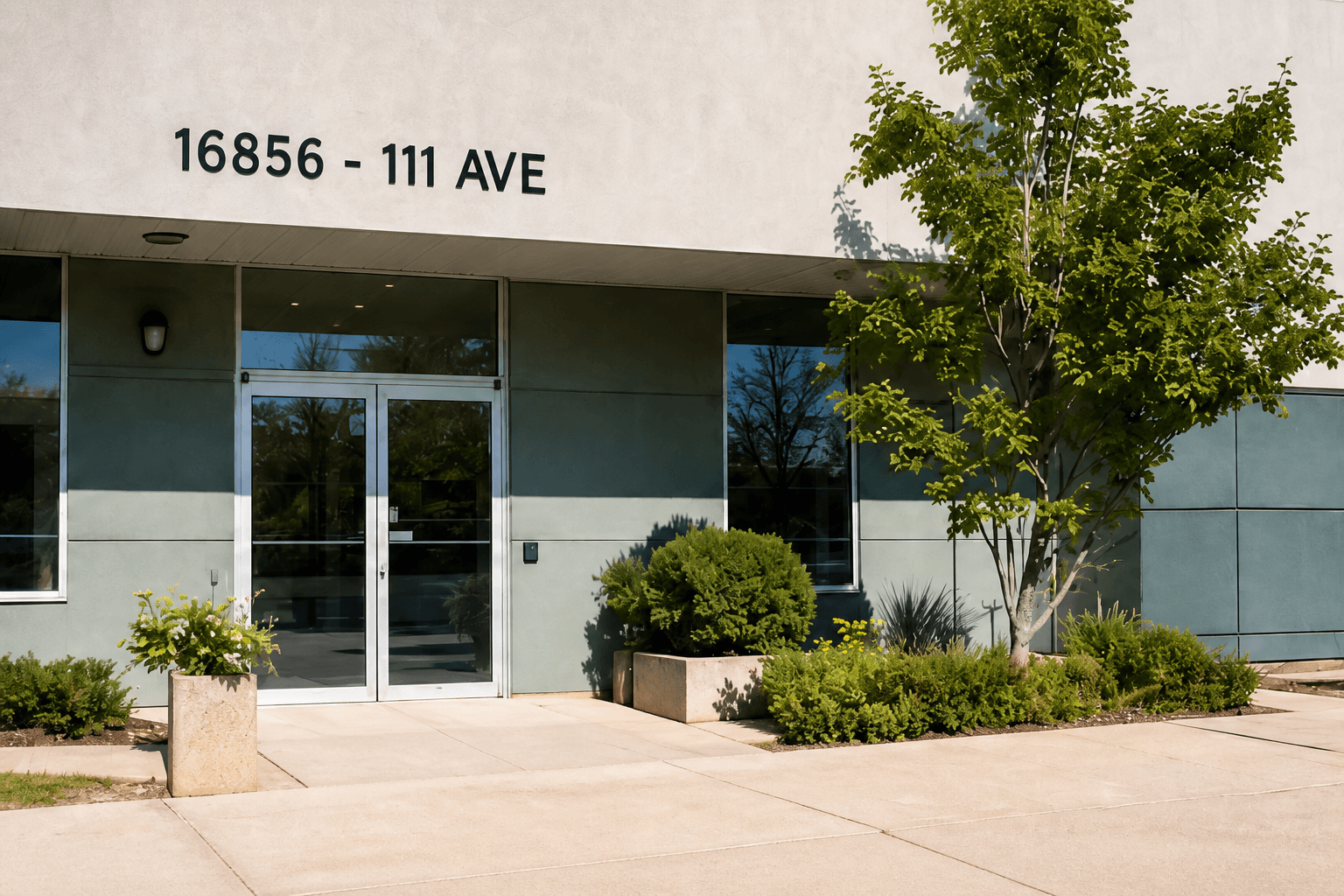 Exterior entrance of the office building at 16856 - 111 Ave, with address lettering above the glass doors, planters and a tree